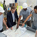 Middle Aged Caucasian Foreman Supervising Multiethnic Team Reviewing Blueprints